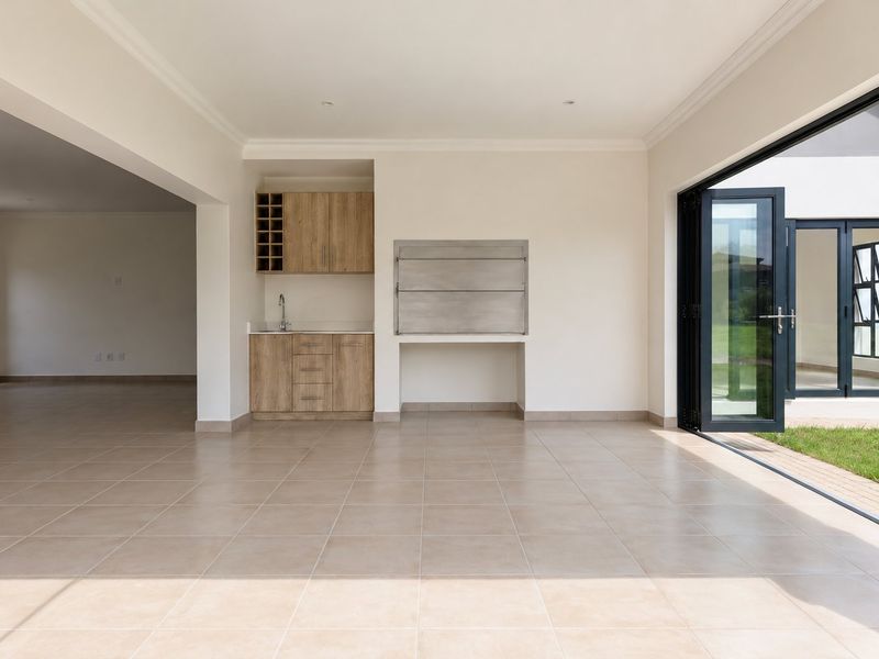 Spacious covered patio featuring a built-in braai, kitchenette with sink, and large stacking doors opening to the garden.