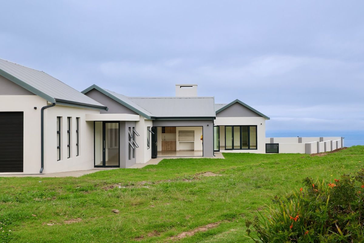 Rear view of a modern single-story home featuring a corrugated metal roof, large sliding glass doors, and a paved patio overlooking the landscape.