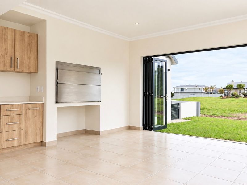 Modern covered patio featuring tiled flooring, built-in cabinetry, and a stainless steel built-in braai, with large bi-fold doors opening to the garden.