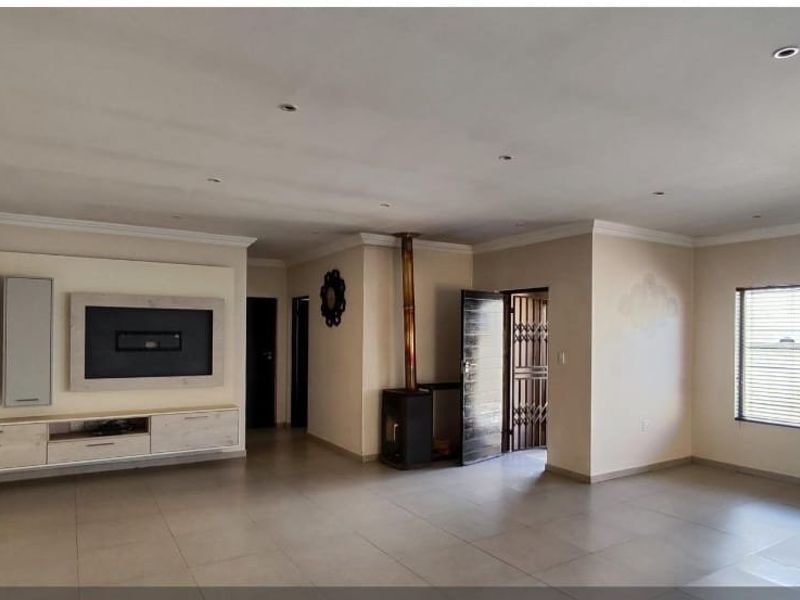 Spacious living area featuring large format floor tiles, a built-in media console, and a freestanding fireplace, offering a versatile open-plan layout.