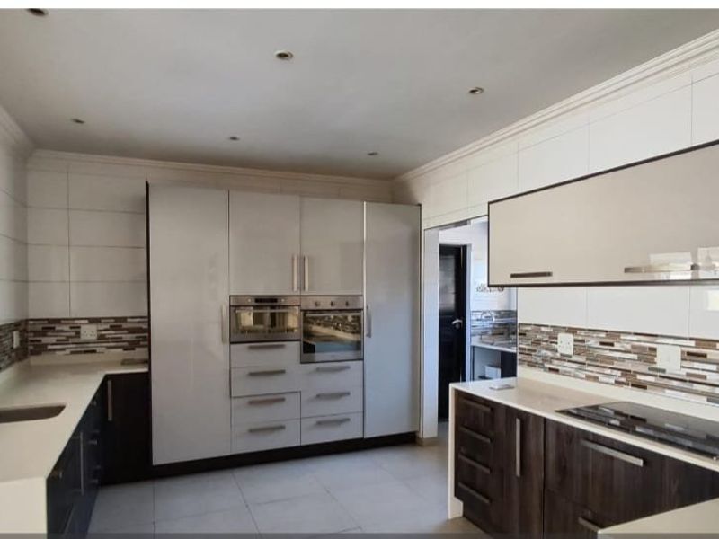 Modern kitchen featuring high-gloss cabinetry, quartz countertops, integrated appliances, and a stylish mosaic tiled backsplash with ample workspace.