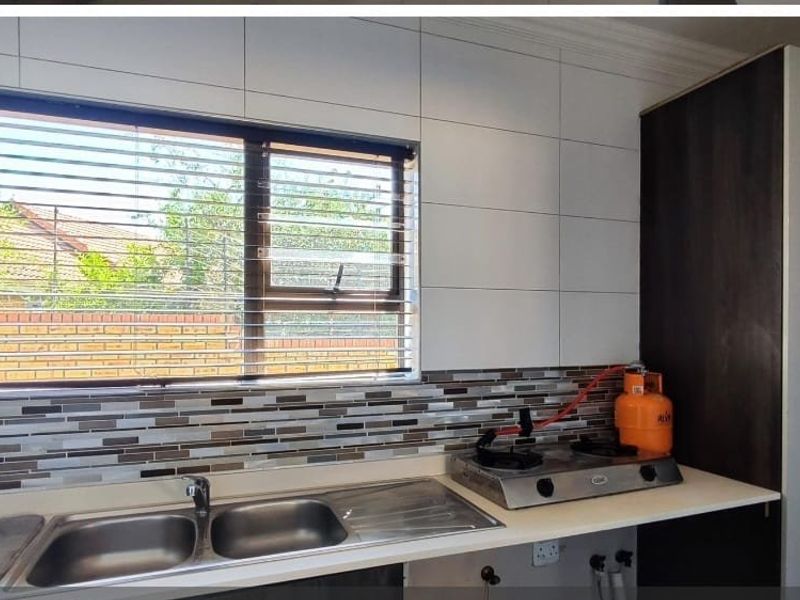 Kitchen area featuring a double stainless steel sink, mosaic tile backsplash, and ample counter space with built-in cabinetry.