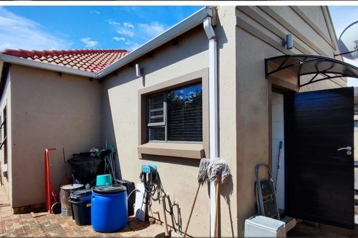 Rear exterior view of the property featuring a paved patio area, external door with canopy, and tiled roof structure.
