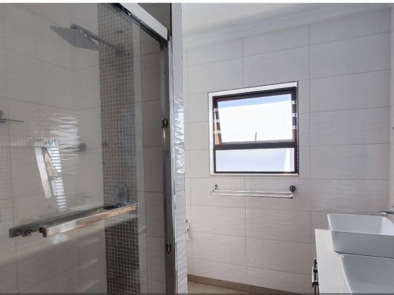 Modern bathroom featuring a glass-enclosed shower with a rain shower head, mosaic tiling, and a double vanity with vessel sinks.
