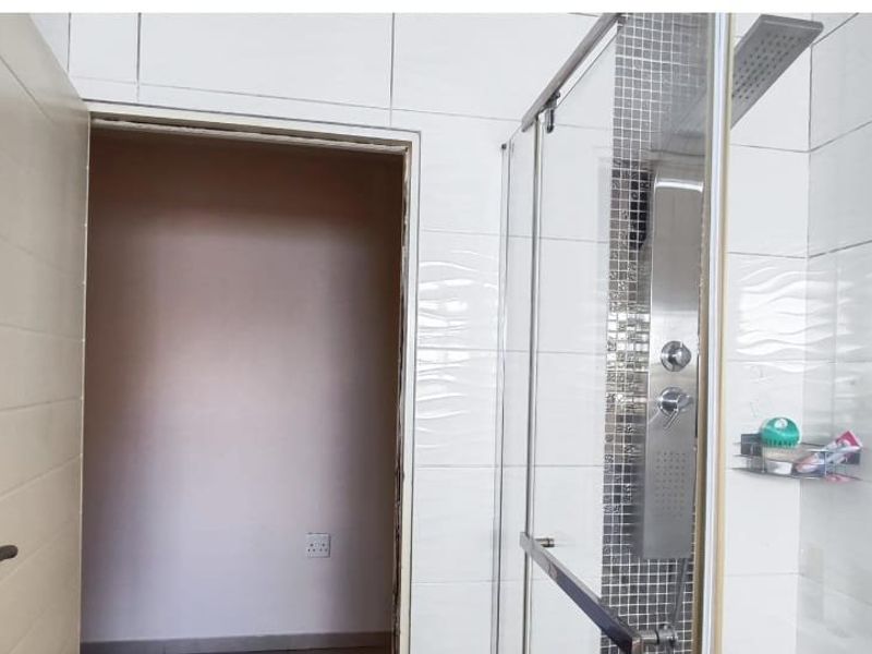 A modern bathroom featuring a glass-enclosed shower with a stainless steel shower panel and tiled walls.
