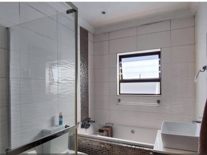 A functional bathroom featuring a glass shower enclosure, a built-in bathtub with mosaic tile detailing, and a modern vessel sink.
