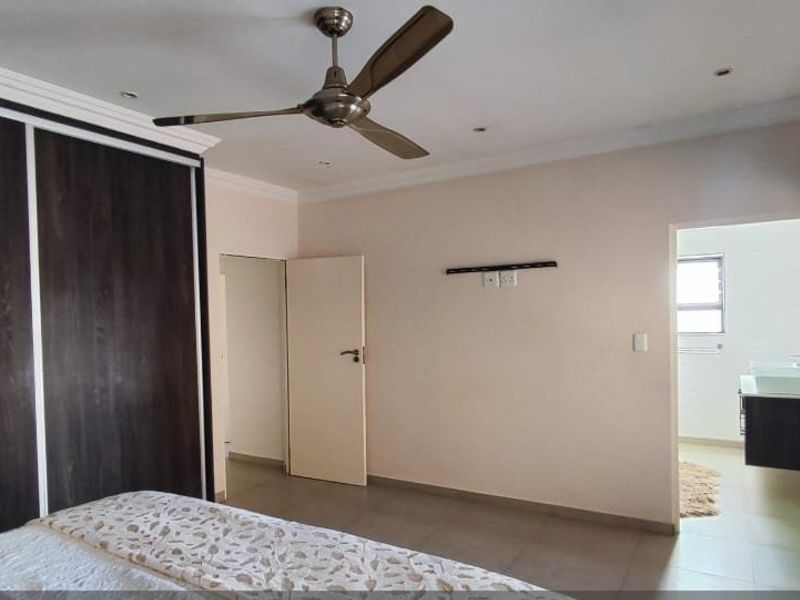 Spacious bedroom featuring built-in cupboards, a ceiling fan, recessed lighting, and an en-suite bathroom with modern vanity.