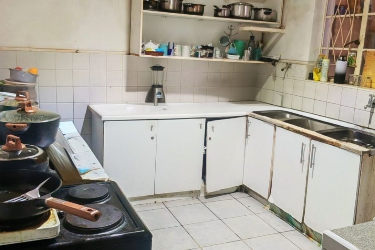 A functional kitchen featuring built-in cabinetry, a double sink, and tiled finishes, currently requiring maintenance and cosmetic updates to improve its overall condition.