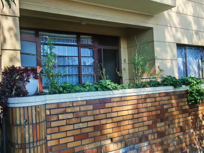 Front elevation of an apartment building featuring a brick facade, a private balcony, and a low brick boundary wall.