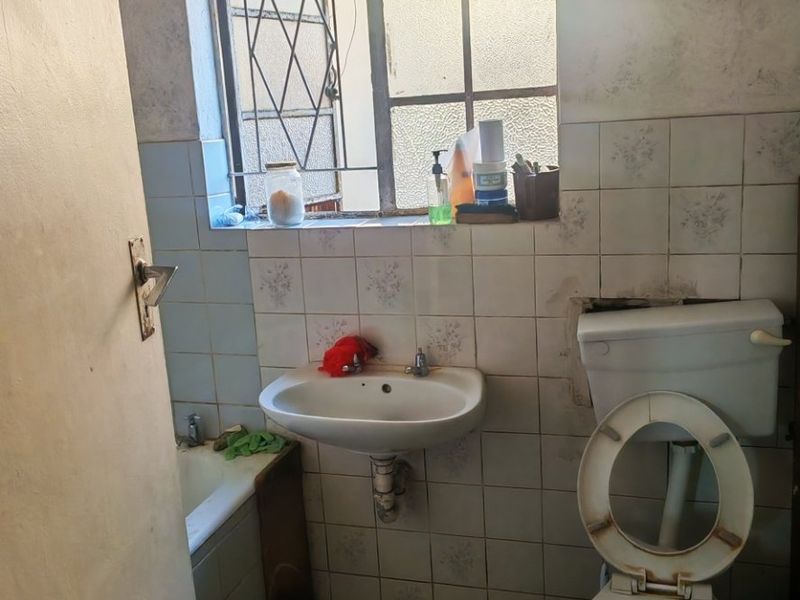 A dated bathroom featuring a pedestal basin, toilet, and bathtub with tiled walls and floors, requiring significant renovation and cosmetic updates.
