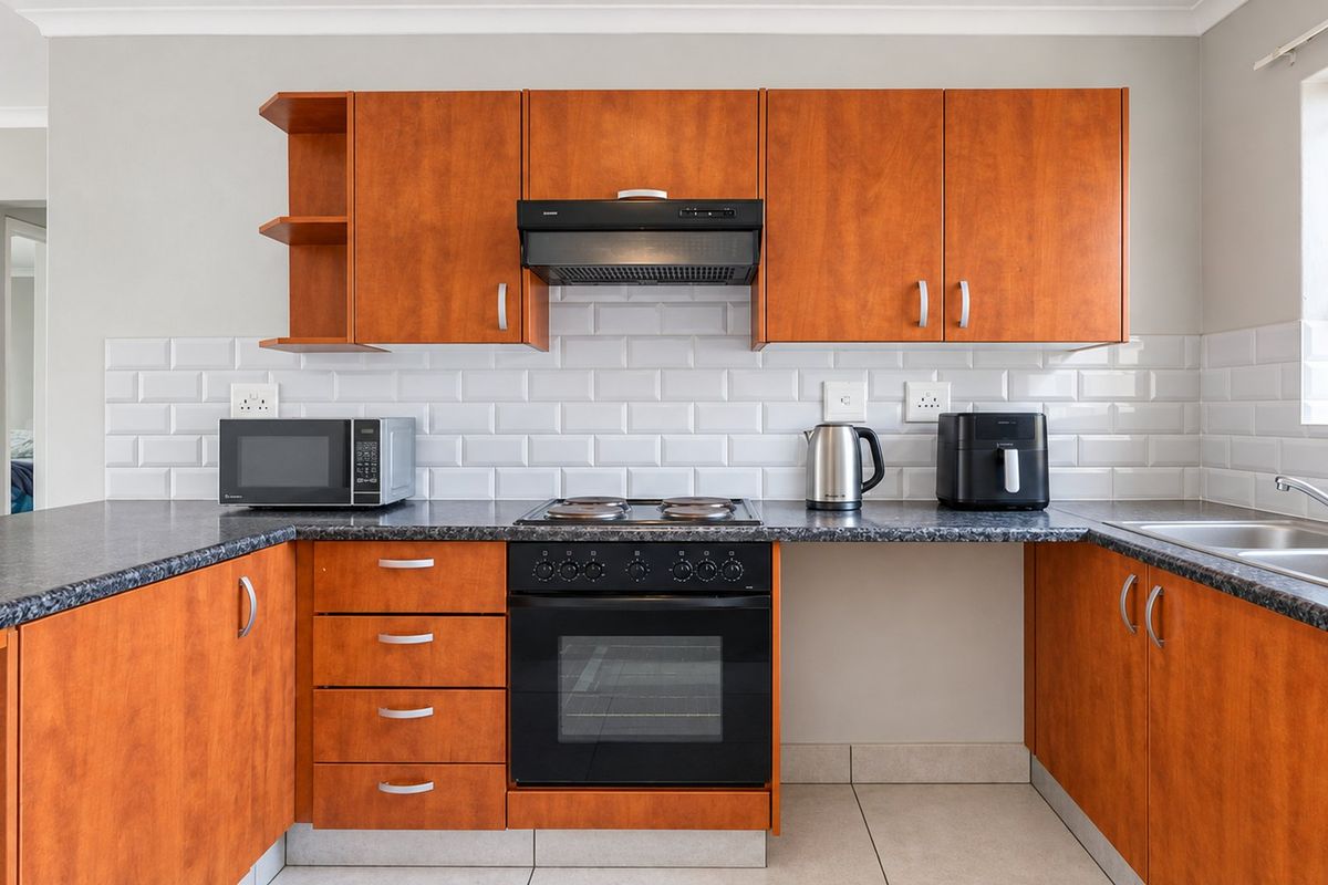 A functional kitchen featuring warm-toned laminate cabinetry, a classic white subway tile backsplash, dark laminate countertops, and a built-in oven with an extractor fan.
