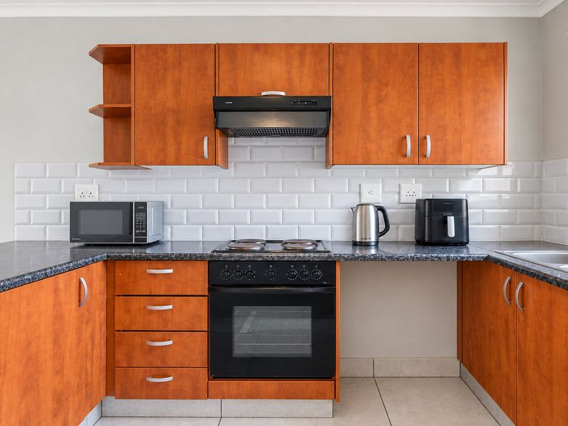 A functional kitchen featuring warm-toned laminate cabinetry, a classic white subway tile backsplash, dark laminate countertops, and a built-in oven with an extractor fan.