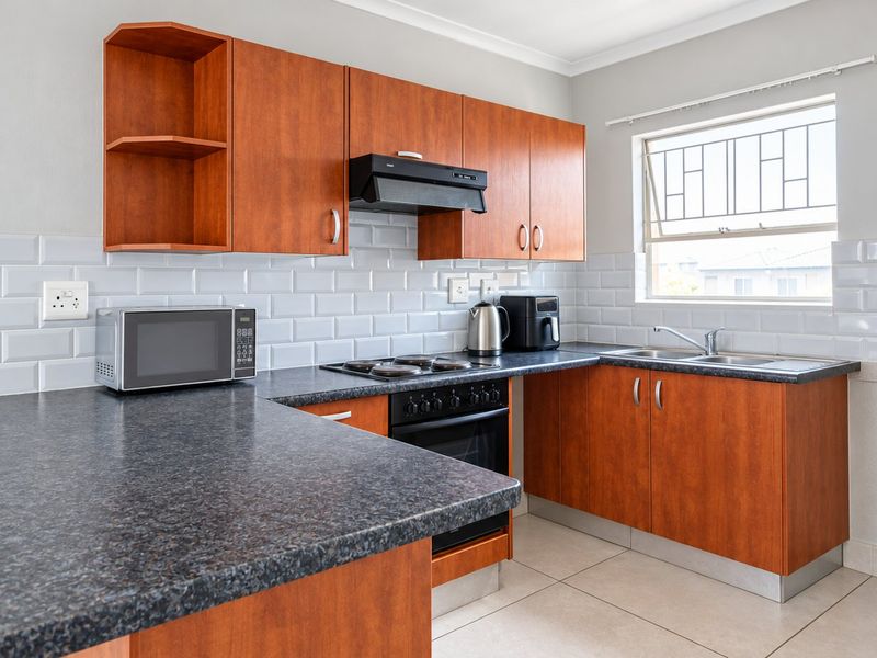 A functional kitchen featuring wood-finish cabinetry, dark laminate countertops, a subway tile backsplash, and integrated cooking appliances.