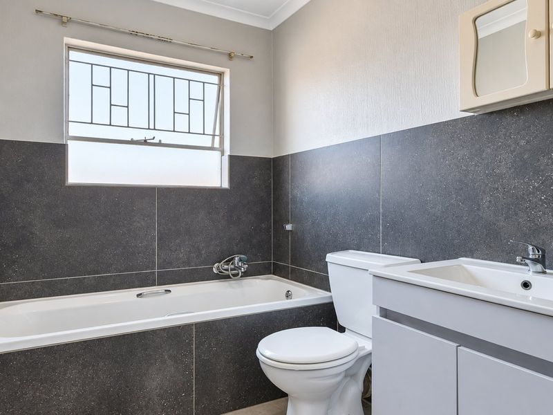 A clean, modern bathroom featuring dark tiled walls, a built-in bathtub, a white vanity with a basin, and a wall-mounted medicine cabinet.