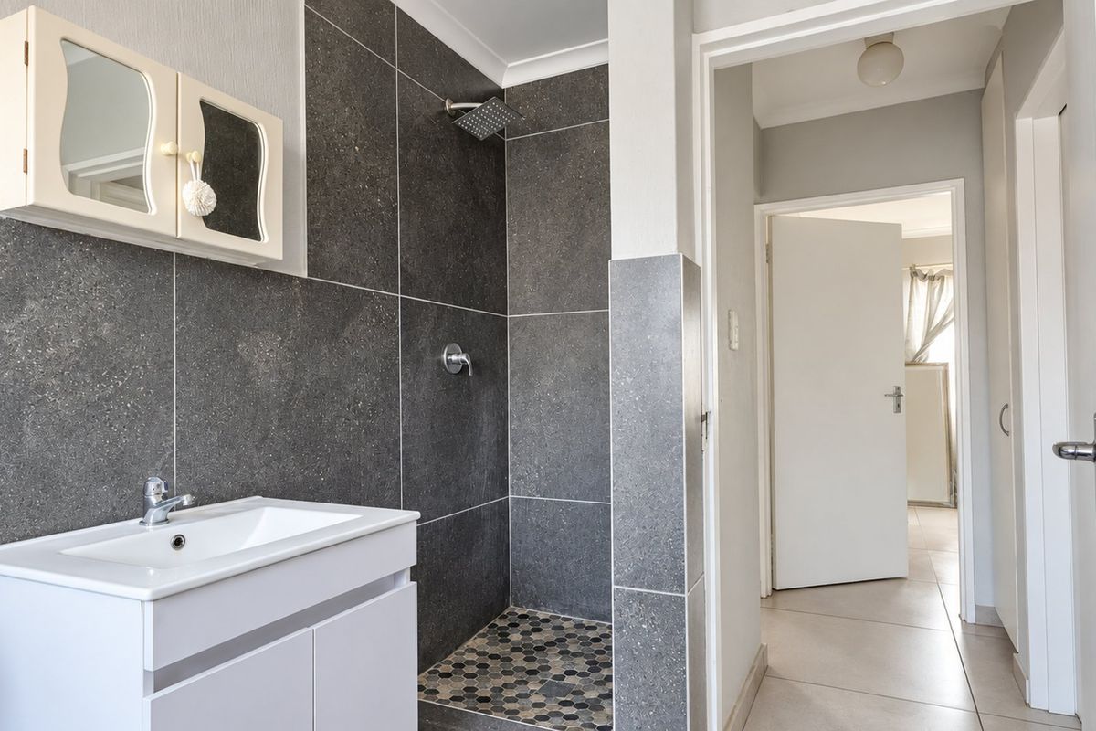 Modern bathroom featuring a walk-in shower with dark grey tiling, a contemporary vanity unit with basin, and neutral floor tiles.