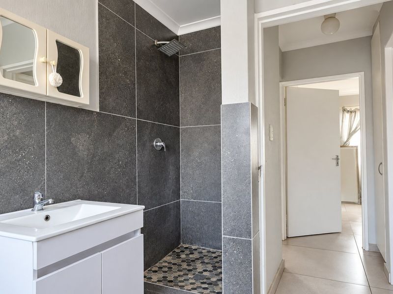Modern bathroom featuring a walk-in shower with dark grey tiling, a contemporary vanity unit with basin, and neutral floor tiles.