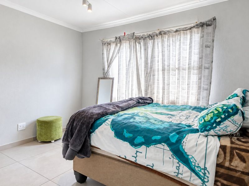 A bright and well-maintained bedroom featuring neutral tiled flooring, clean wall finishes, and a ceiling-mounted spotlight fixture.