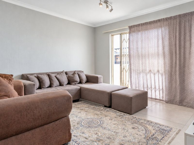 A well-lit living room featuring neutral tiled flooring, coved ceilings, and a sliding glass door with an integrated security gate leading to the exterior.