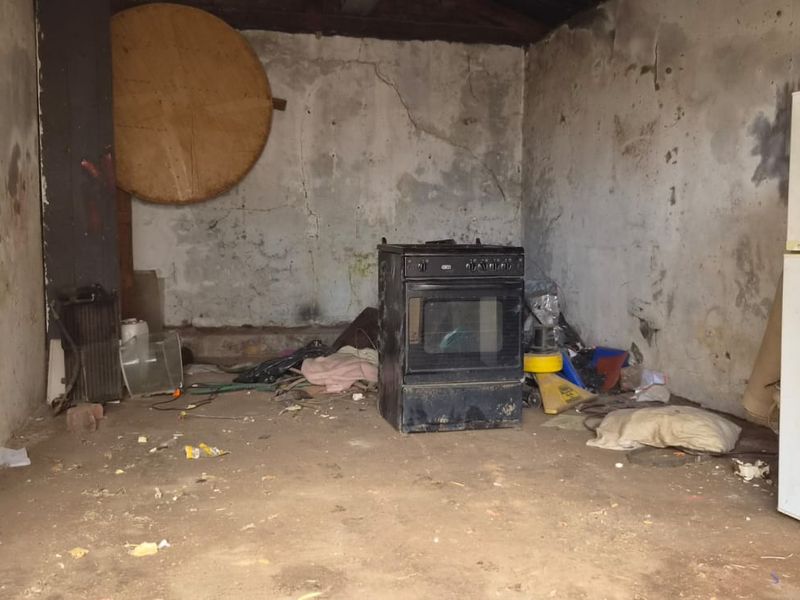 A dilapidated utility space or storage area featuring unfinished walls with significant surface damage and a concrete floor.