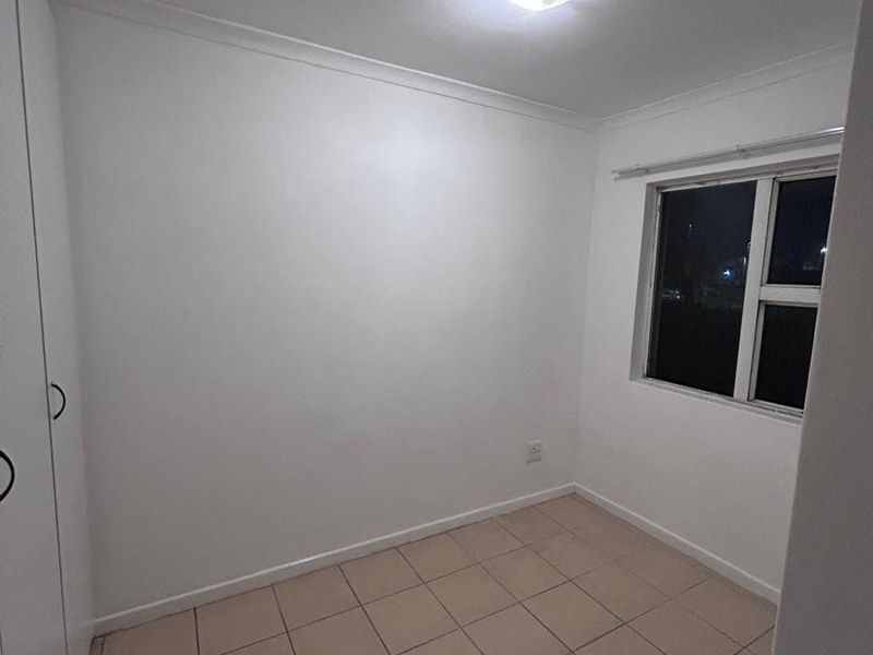 A clean, empty bedroom featuring tiled flooring, a built-in wardrobe, and a window, providing a neutral space ready for personalization.