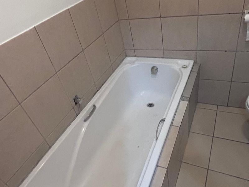 A functional bathroom featuring a built-in bathtub with tiled surround and flooring, currently requiring minor repairs and cosmetic updates.