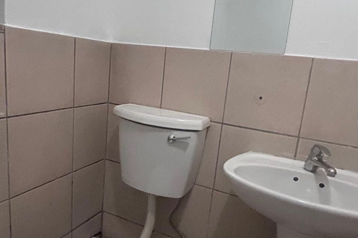 A compact bathroom featuring a pedestal basin, toilet, and wall-mounted mirror with neutral ceramic wall tiling.