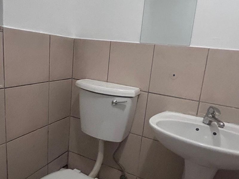 A compact bathroom featuring a pedestal basin, toilet, and wall-mounted mirror with neutral ceramic wall tiling.