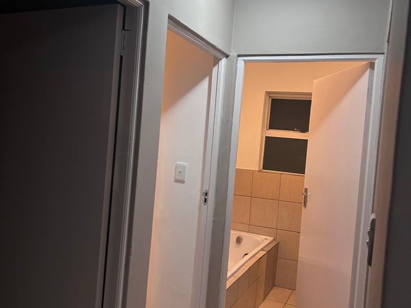 A functional hallway providing access to the bathroom, featuring neutral wall tones, tiled flooring, and standard internal door fixtures.