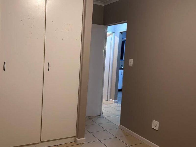 An empty bedroom featuring built-in cupboards, tiled flooring, and neutral wall paint, with a view through to an adjacent hallway.