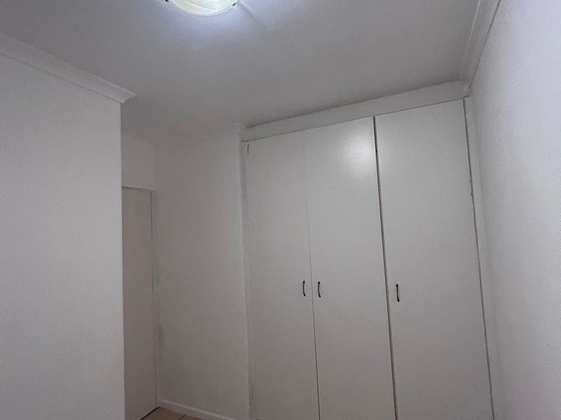 A clean, empty bedroom featuring neutral tiled flooring and ample built-in cupboard storage space.