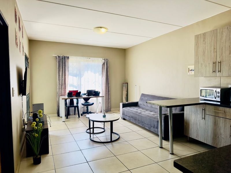 Open-plan living area featuring tiled flooring, a functional kitchen with built-in cabinetry, a breakfast bar, and a bright window with security gate.