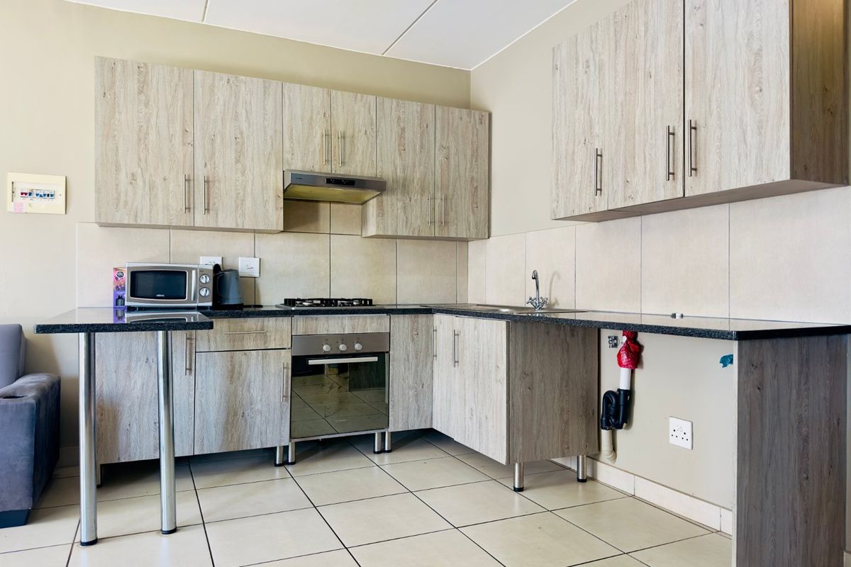 A functional kitchen featuring wood-look cabinetry, granite-style countertops, a built-in oven with gas hob, and tiled finishes throughout.