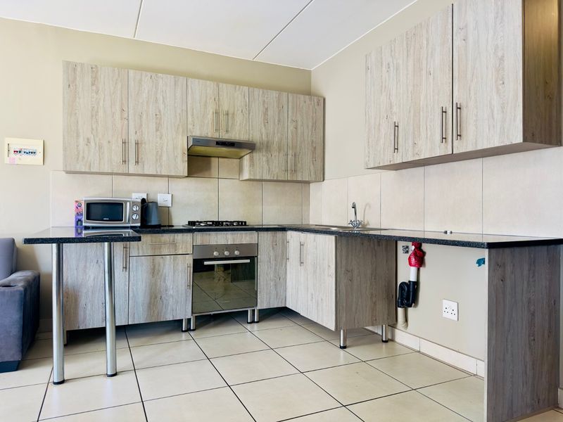 A functional kitchen featuring wood-look cabinetry, granite-style countertops, a built-in oven with gas hob, and tiled finishes throughout.