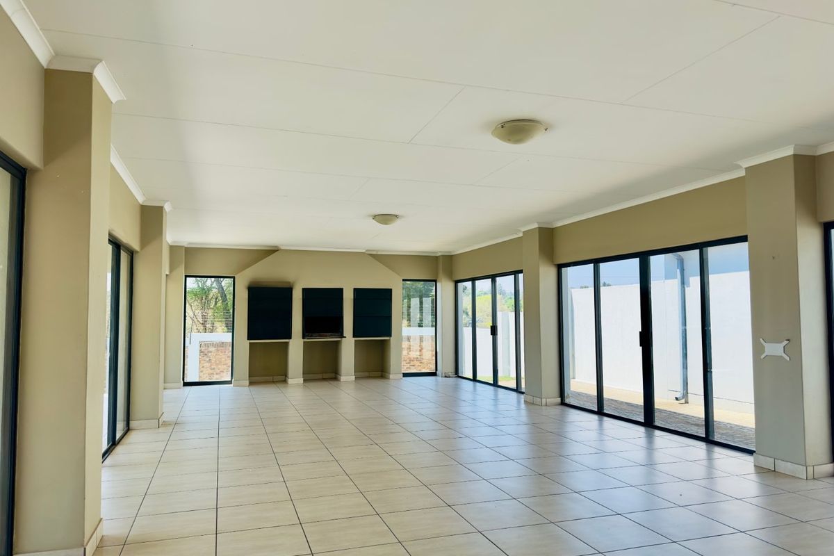 A spacious, open-plan living area featuring neutral tiled flooring, extensive sliding glass doors for natural light, and built-in wall shelving.