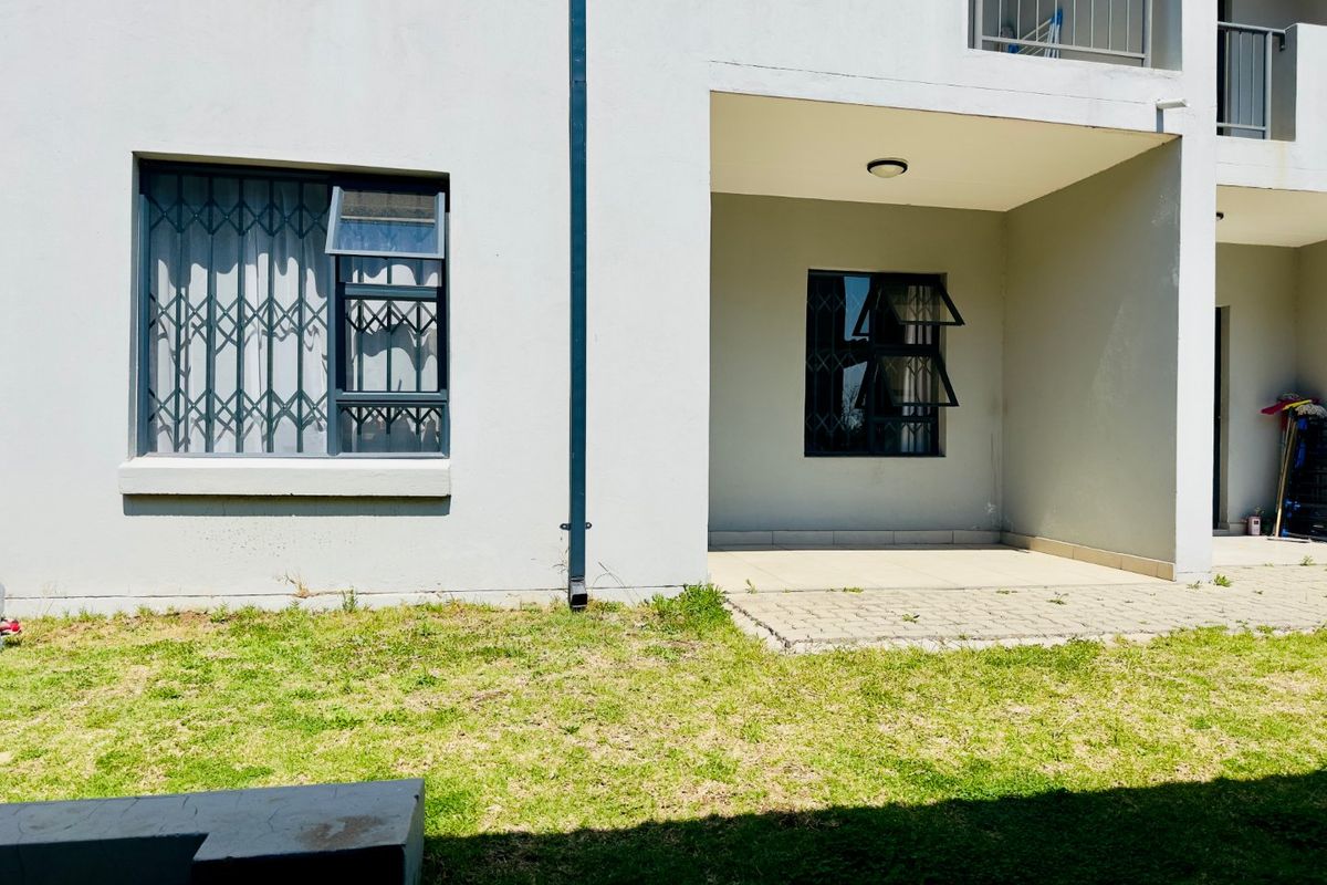 Rear view of the apartment building featuring a ground floor tiled patio, security gates on windows, and a small private garden area.