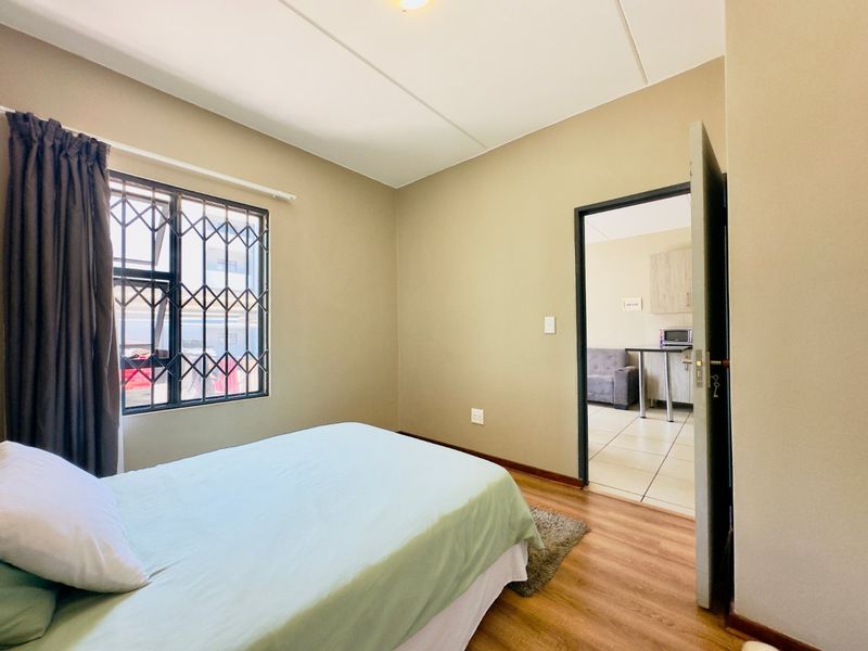 A bedroom featuring laminate flooring and a security gate on the window, with an open doorway leading to an adjacent living area.