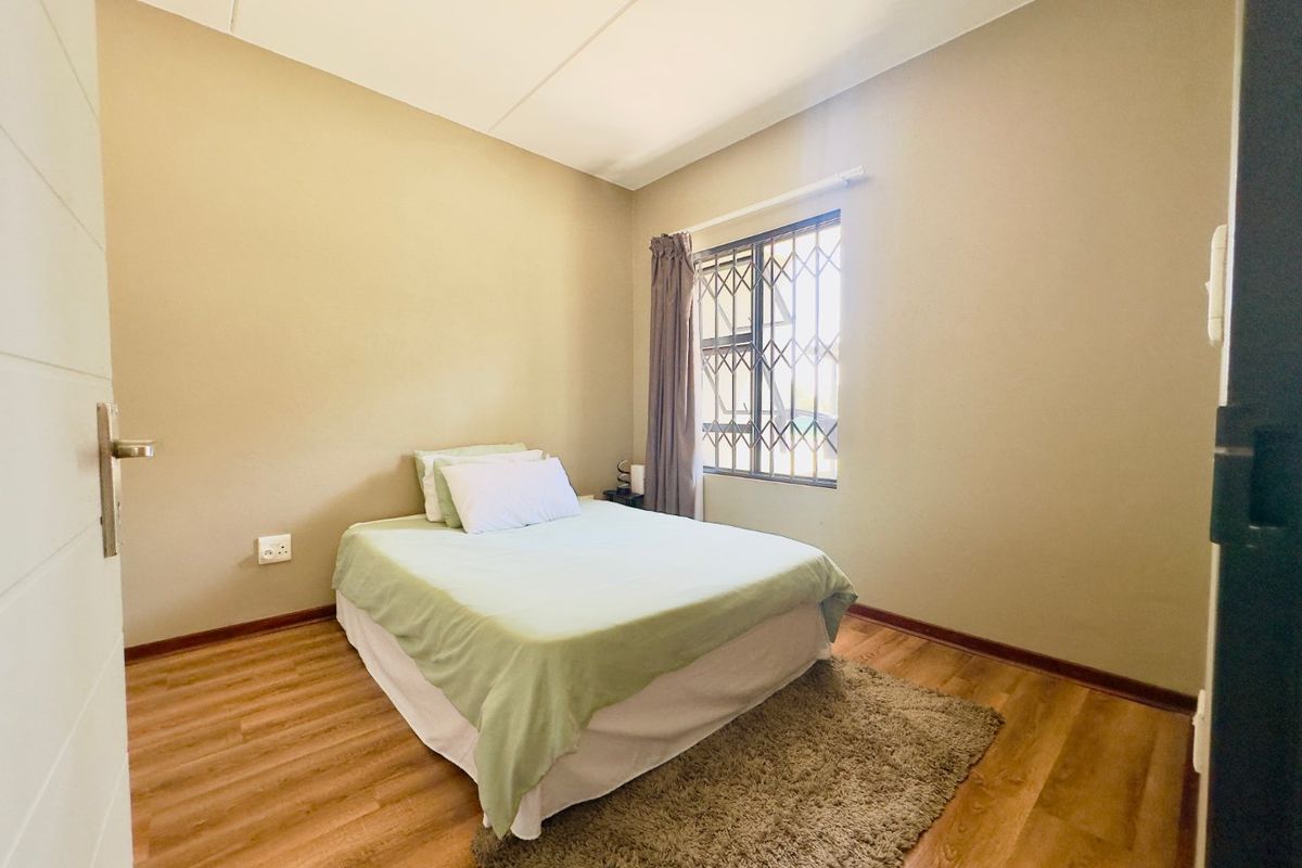 A bedroom featuring laminate flooring, neutral wall tones, and a window fitted with a security gate.