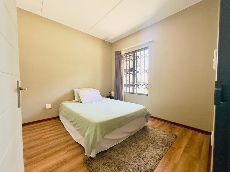A bedroom featuring laminate flooring, neutral wall tones, and a window fitted with a security gate.
