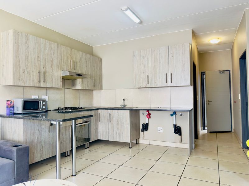 Functional kitchen featuring light wood-grain cabinetry, granite countertops, built-in oven and hob, and tiled flooring, with an adjacent hallway entrance.