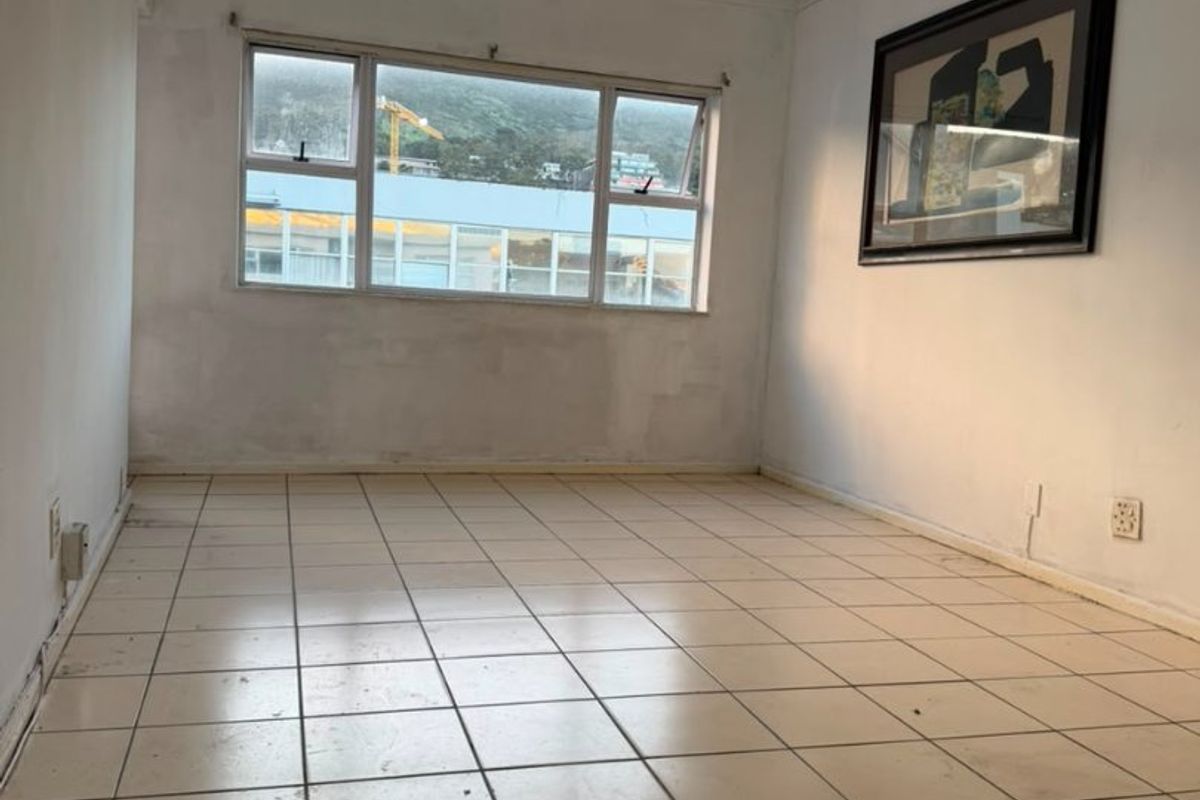An empty living room featuring ceramic floor tiles, a ceiling fan, and large windows with natural light.