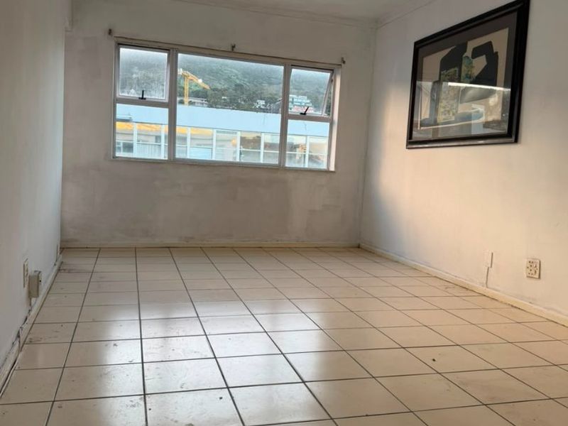 An empty living room featuring ceramic floor tiles, a ceiling fan, and large windows with natural light.