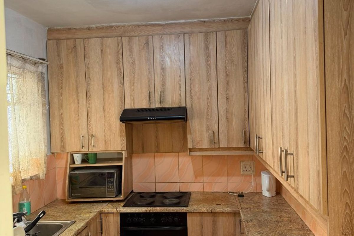 Compact kitchen featuring wood-look laminate cabinetry, stone-effect countertops, built-in oven, electric hob, and tiled backsplash.