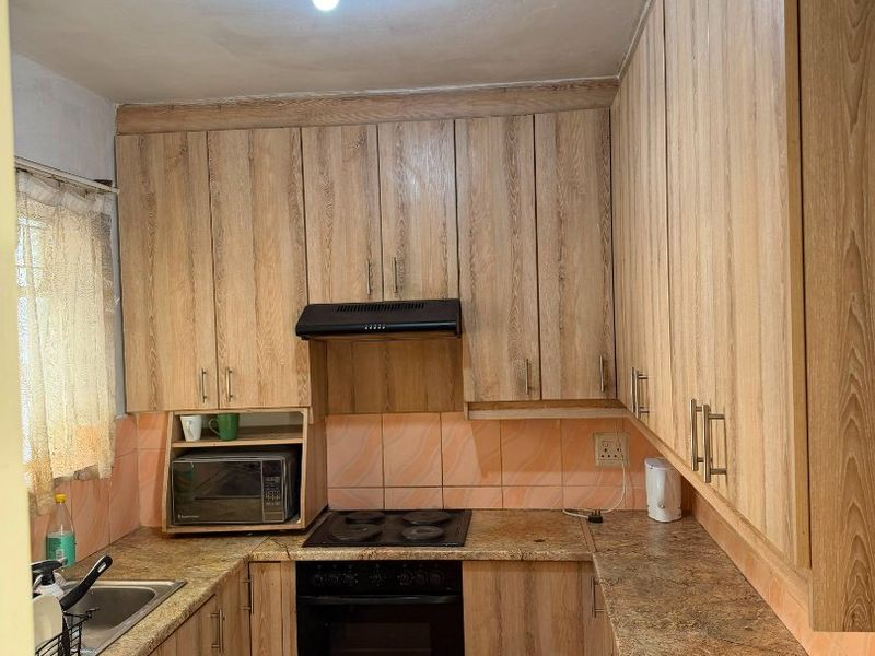 Compact kitchen featuring wood-look laminate cabinetry, stone-effect countertops, built-in oven, electric hob, and tiled backsplash.