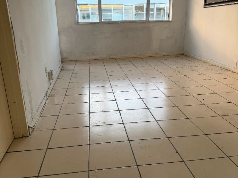 An empty living room featuring tiled flooring and a large window, currently requiring cosmetic updates to the wall finishes.