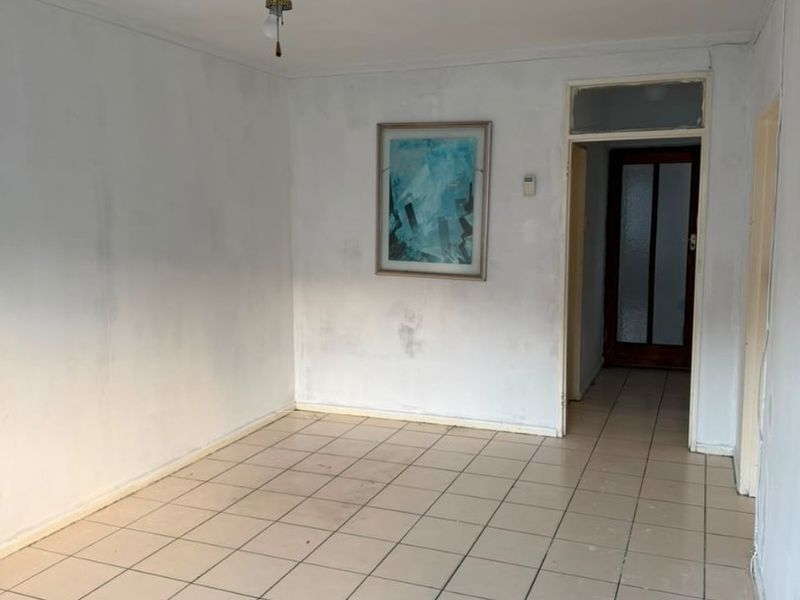An empty living room featuring tiled flooring and a ceiling fan, requiring cosmetic updates to the walls and flooring.