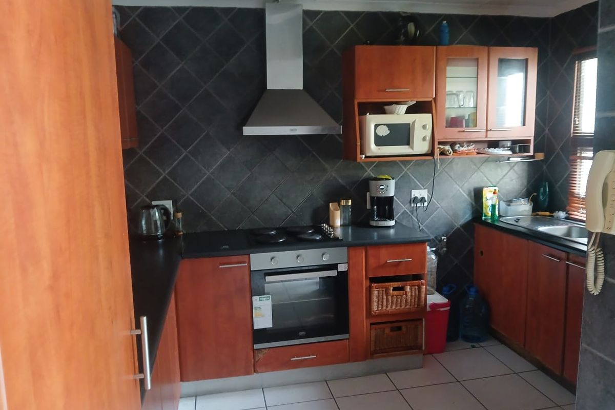 Functional kitchen featuring wood-finish cabinetry, dark tiled backsplash, built-in oven and hob, and tiled flooring.