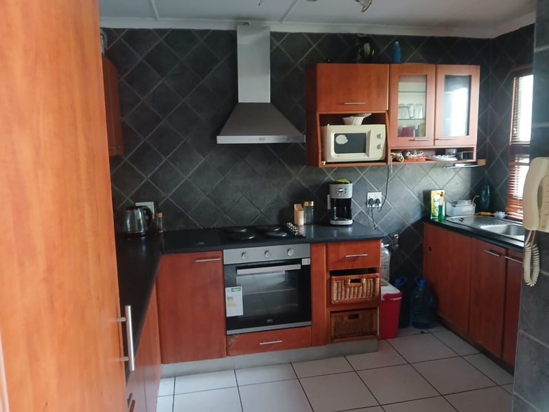 Functional kitchen featuring wood-finish cabinetry, dark tiled backsplash, built-in oven and hob, and tiled flooring.