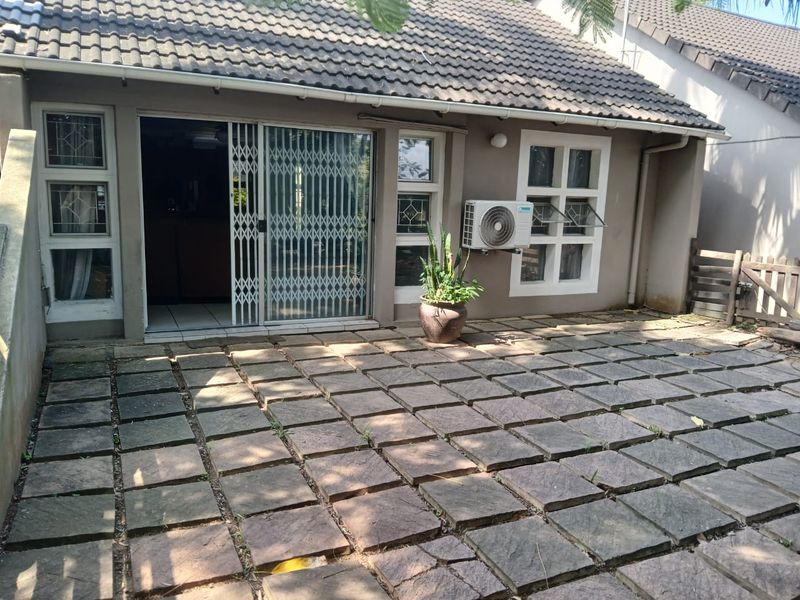 Rear exterior view of the townhouse featuring a paved patio area, sliding door access with security gate, and an external air conditioning unit.