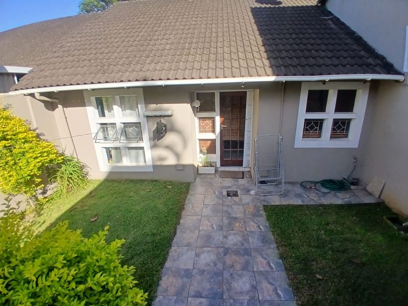 Rear exterior view of the townhouse featuring a tiled walkway, garden area, and access door with casement windows.