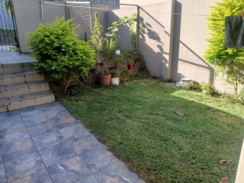 A compact rear garden area featuring a tiled patio, concrete steps, and a retaining wall, providing a functional outdoor space for the townhouse.